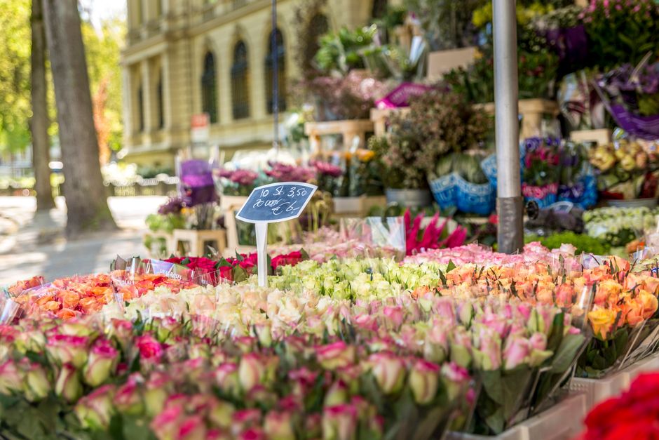A vibrant outdoor flower stall featuring an array of fresh flowers arranged in bouquets and bundles. Prominent among them are pink and white roses, along with orange and peach blooms, all carefully wr